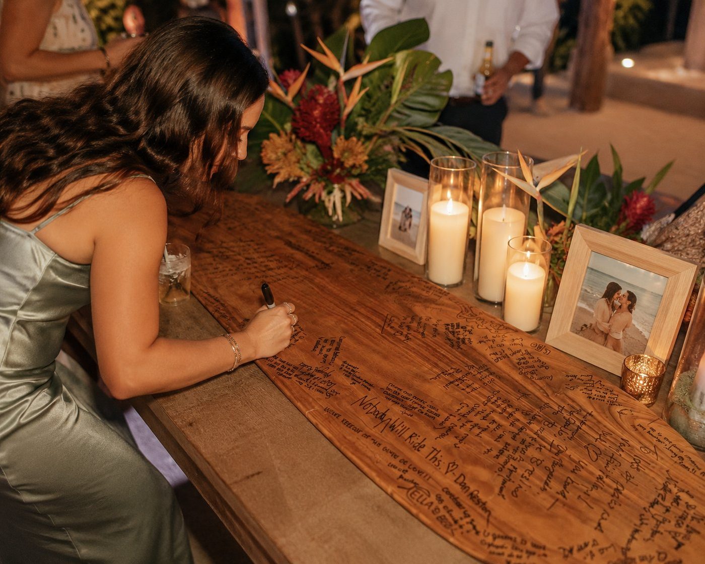 Wedding guest signing the handcrafted alaia guest book with candles and tropical florals