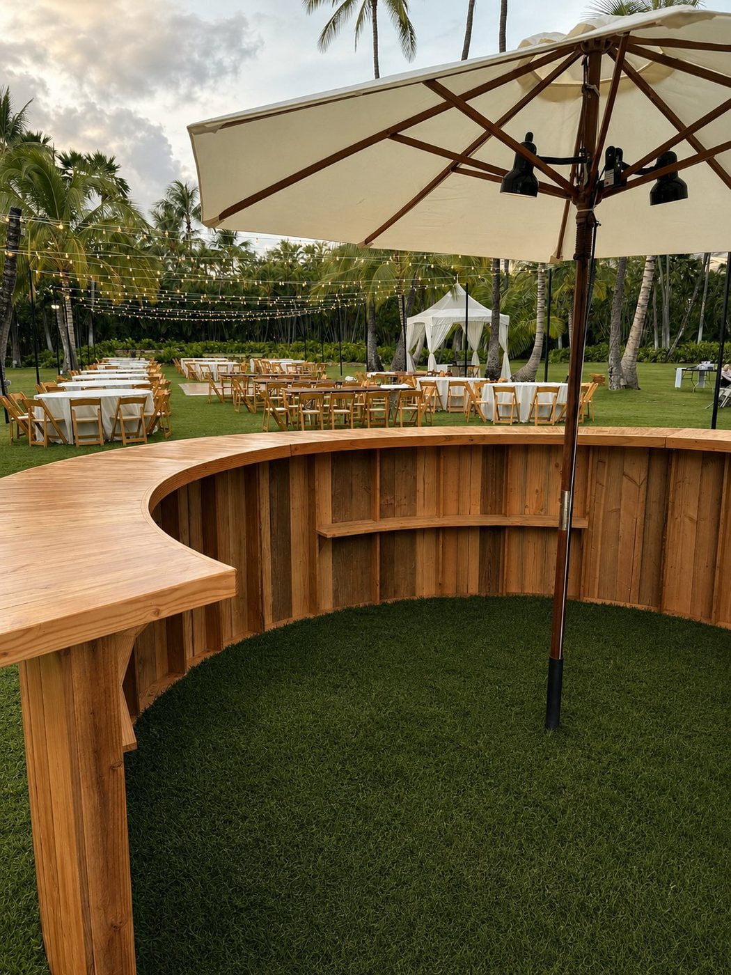 Light wood semi-circle bar with white market umbrella and string lights at an outdoor reception