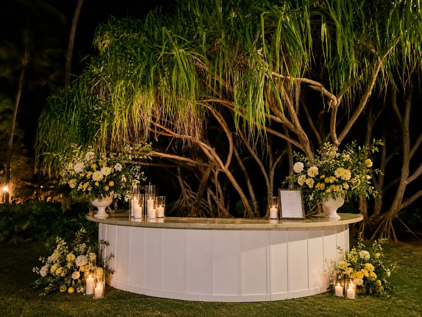 White semi-circle bar at night with candles and yellow and green florals at LouLou Palms